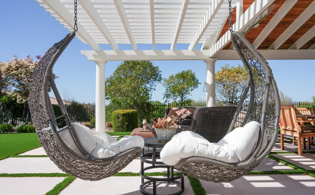Paver patio with turf joints and hanging swing chairs under a pergola by Be Home Remodeling
